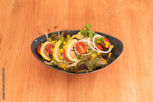 A long tray with a salad of lettuce, sweet corn, cherry tomatoes, rings of raw white onion and lemon wedges