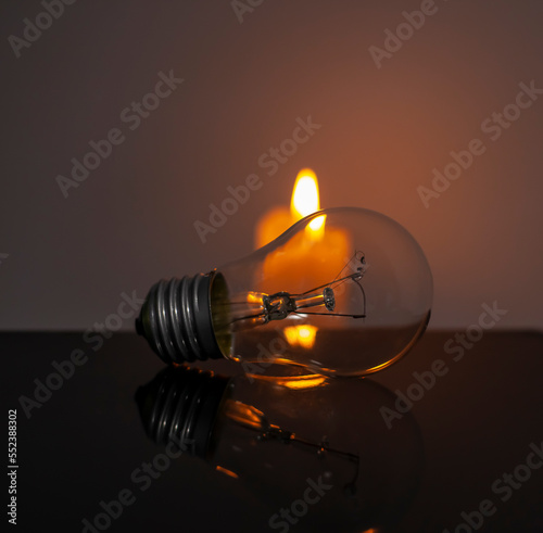 Burning candle near a switched off light bulb in complete darkness. Blackout, electricity off, energy crisis or power outage, concept image