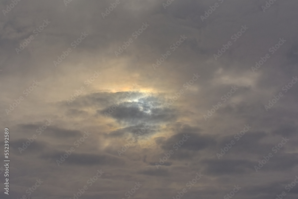 Bright yellow sun shining through ominous dark grey clouds in the sky Bright yellow sun shining through ominous dark grey clouds in the sky