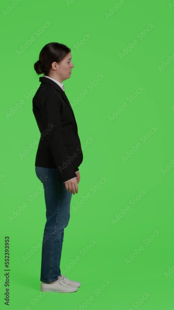 Vertical video: Profile of negative mad office worker showing disapproval on camera, acting angry and furious standing over full body greenscreen backdrop. Young woman expressing disagreement in Vertical video: Profile of negative mad office worker showing disapproval on camera, acting angry and furious standing over full body greenscreen backdrop. Young woman expressing disagreement in
