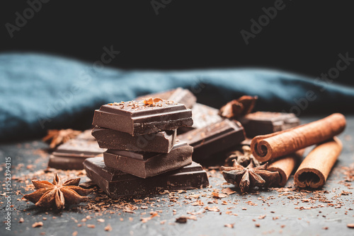 Dark chocolate bar pieces on dark background with copy-space, grated chocolate and spices, pile chunks of broken chocolate
