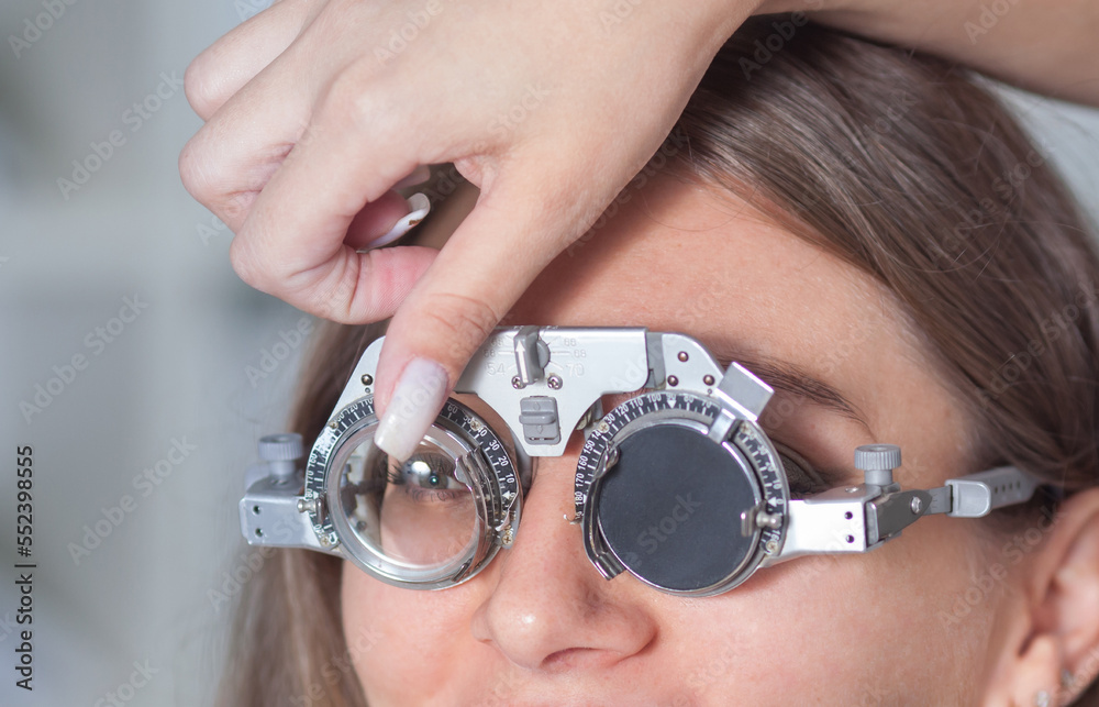 Fototapeta premium a young optometrist girl holds a trial eyeglass frame in her hands, and tries it on to a female patient, the concept of glasses selection, vision correction.