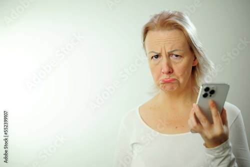 upset cute woman blond hair childishly offended Sad adult woman holding smartphone, looking upset with regret, standing in tshirt against white background phone woman stick out her lip photo