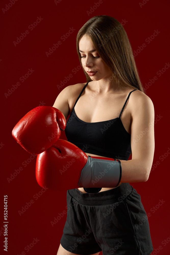 Portrait of pretty woman in black wearing boxer gloves on red studio background. Seductive sporty female preparing hands for box training. Concept of professional uniform and women in sport. Portrait of pretty woman in black wearing boxer gloves on red studio background. Seductive sporty female preparing hands for box training. Concept of professional uniform and women in sport.