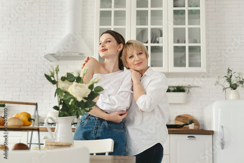 Close-up portrait of two nice attractive lovely tender cheerful women mom mommy adult daughter spending time day together in white light interior house flat apartment indoors