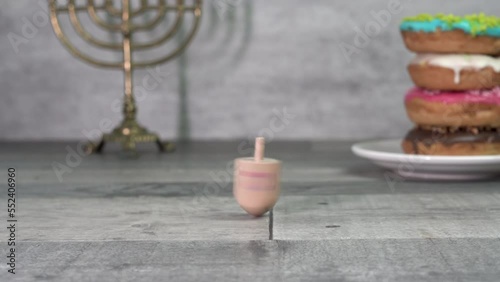 Hand twists a dreidel with the letters Shin, Hey, Nun and Gimel (Hebrew). In the background are hanukkah and donuts. Hanukkah. Jewish holidays (152)