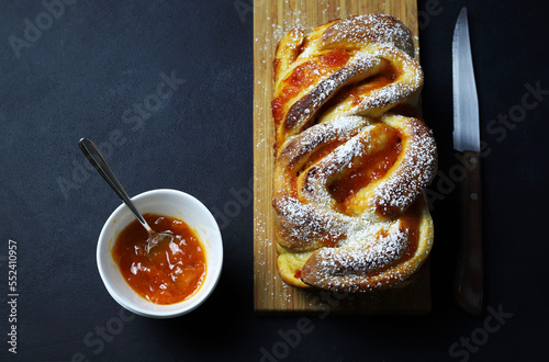 Babka o pane brioche con marmellata di albicocche su sfondo scuro. Pane intrecciato o arrotolato. Dolci fatti in casa per la colazione. photo