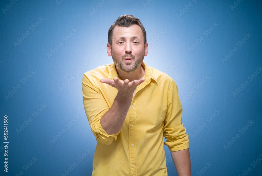Lovely young man send kiss to you over blue background, dresses in yellow shirt. Handsome lovely guy kissing Lovely young man send kiss to you over blue background, dresses in yellow shirt. Handsome lovely guy kissing