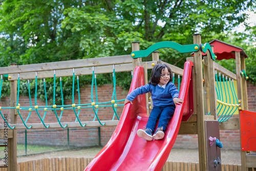 Handsome active little boy having fun while playing and sliding on the outdoor playground. Kids play on school or kindergarten colorful yard. Healthy summer activity for children.