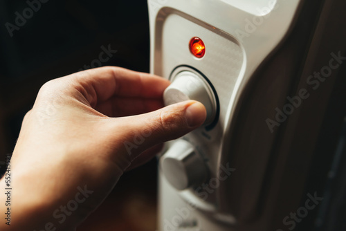 Man adjusting the oil electric heater on at home. Cold winter, economic crisis concept. 