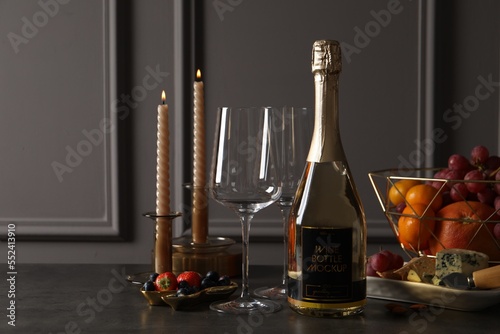 Bottle of sparkling wine, glasses, candles and delicious snacks on grey table