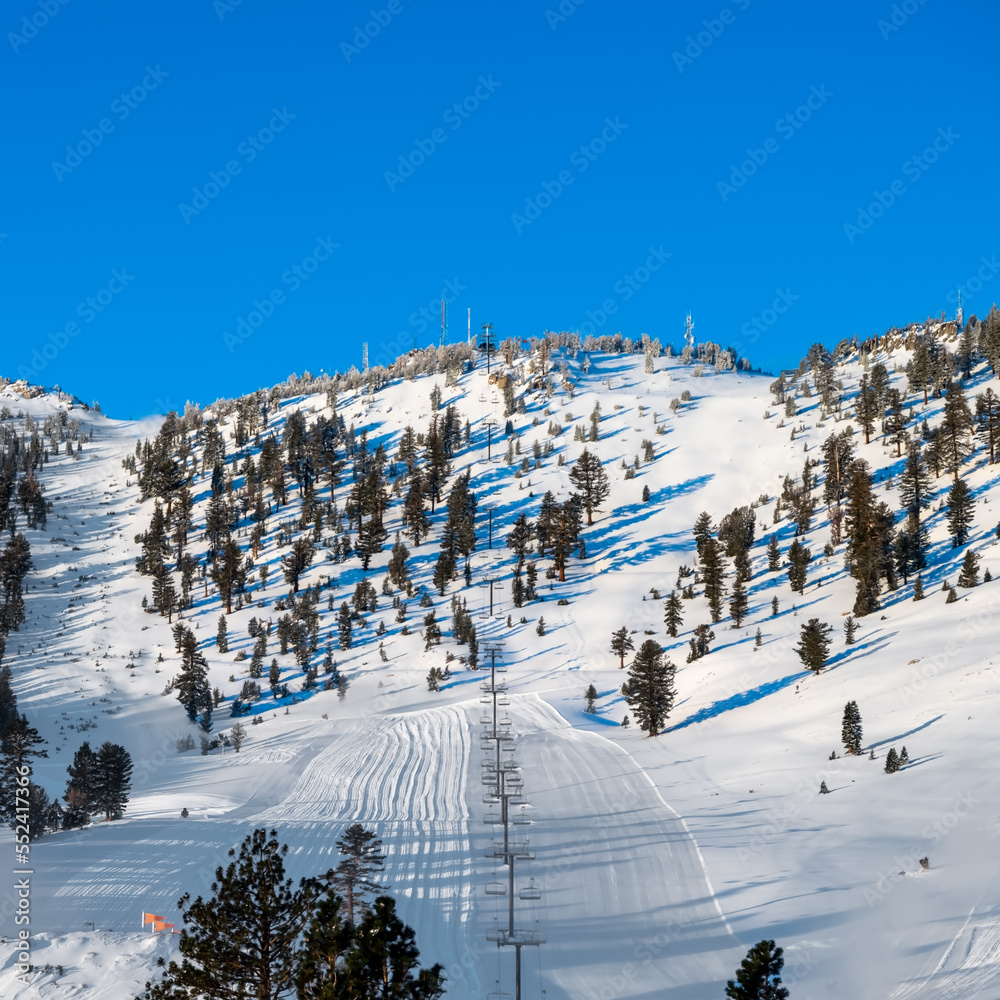 Fresh groomed ski run with a ski chairlift on a steep snowcapped mountain
