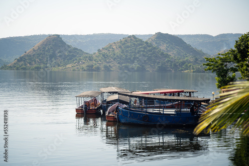 boats moored tied on Dhebar lake with Aravalli hills in the distance at dusk showing the beautiful view of asia's largest manmade lake and popular tourist and holiday destination photo