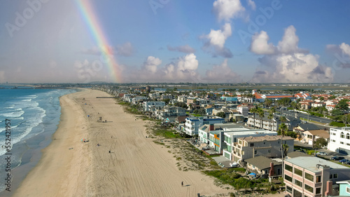 aerial shot of the coastline with blue ocean water and homes along the sand on the beach, cars driving on the street and blue sky, clouds and a rainbow in Huntington Beach California USA photo