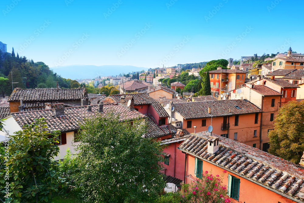 View from above of the Italian city: you can see the roofs of houses, pink and orange stucco, in the distance - the mountains.