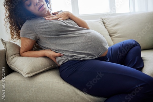 Pregnant woman sitting on the couch lower back pain and headache, strain on the spine during pregnancy. Lifestyle difficulties of motherhood preparation for childbirth, the last month of pregnancy