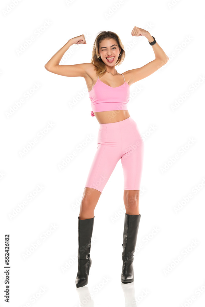 a young happy woman in pink short leggings and top, and black leather boots on a white background a young happy woman in pink short leggings and top, and black leather boots on a white background