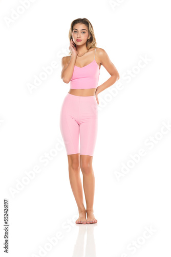 a young barefeet woman in pink short leggings and top posing on a white studio background