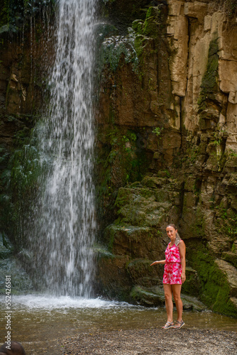 Fototapeta Naklejka Na Ścianę i Meble -  one girl in a pink dress stands at a waterfall
