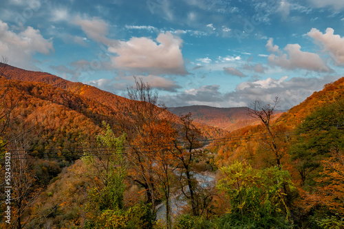 Mountain autumn landscape with colorful forest and river. Trees with bright yellow-red foliage on the rocks. Autumn view of the river flowing between the mountains.