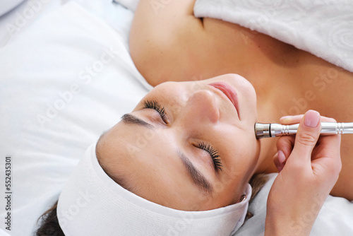 The cosmetologist makes the procedure Microdermabrasion of the skin of the face of a beautiful, young woman in a beauty salon. Cosmetology and professional skin care.
