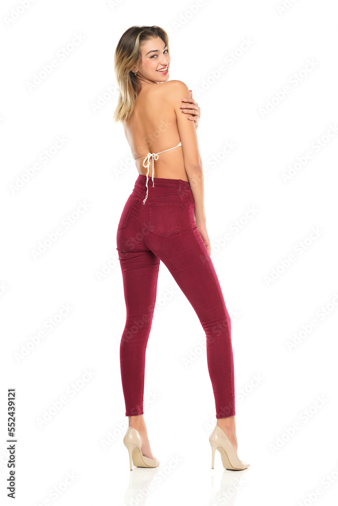 a young smiling woman in burgundy jeans and top, and high heels shoes posing on a white background. Rear, back view