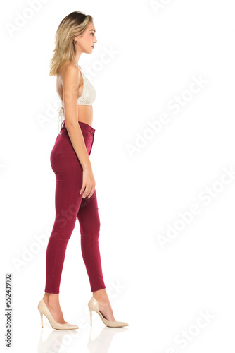 a young woman in burgundy jeans and top, and high heels shoes posing on a white background. Side profile view