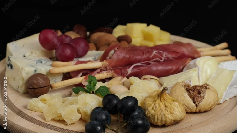Cheese plate with camembert brie parmesan maasdam dutch cheese. Assortment of spanish or italian antipasti snack with cheese, nuts, bread, grapes, dates, figs. Top view flat lay background slow motion Cheese plate with camembert brie parmesan maasdam dutch cheese. Assortment of spanish or italian antipasti snack with cheese, nuts, bread, grapes, dates, figs. Top view flat lay background slow motion