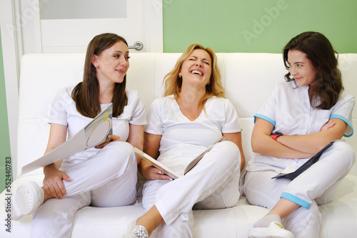 Fotografi Colleagues cosmetologists in white uniforms sit together on the couch during a break and laugh