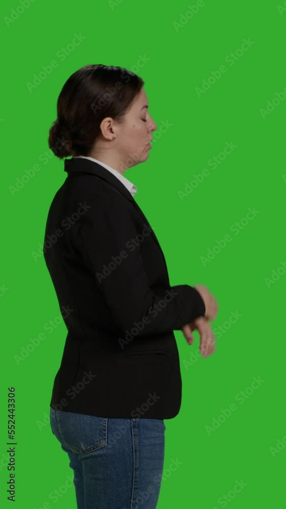 Vertical video: Profile close up of impatient office worker checking time on wristwatch, standing over isolated greenscreen backdrop. Young woman running late and looking at clock, waiting for Vertical video: Profile close up of impatient office worker checking time on wristwatch, standing over isolated greenscreen backdrop. Young woman running late and looking at clock, waiting for