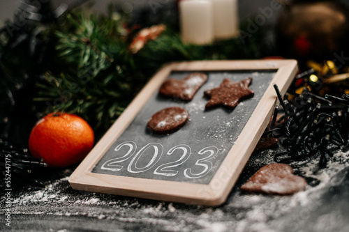 New Year sign 2023. Baking Christmas gingerbread cookies on a dark wooden table. Christmas lights in background. Winter holidays. Top view. Shallow depth of field. 