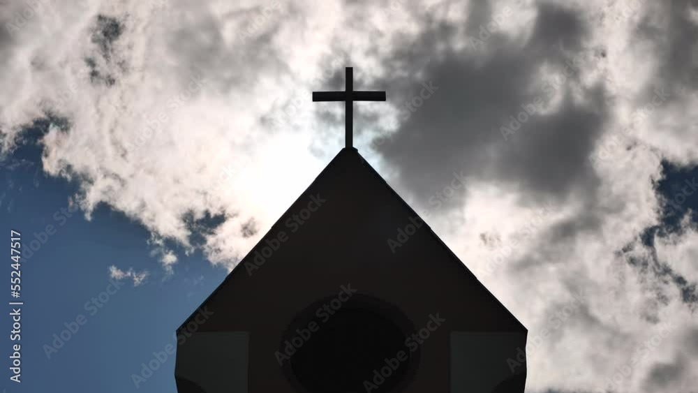 The silhouette of a Catholic church tower against a background of sun and clouds. The silhouette of a Catholic church tower against a background of sun and clouds.