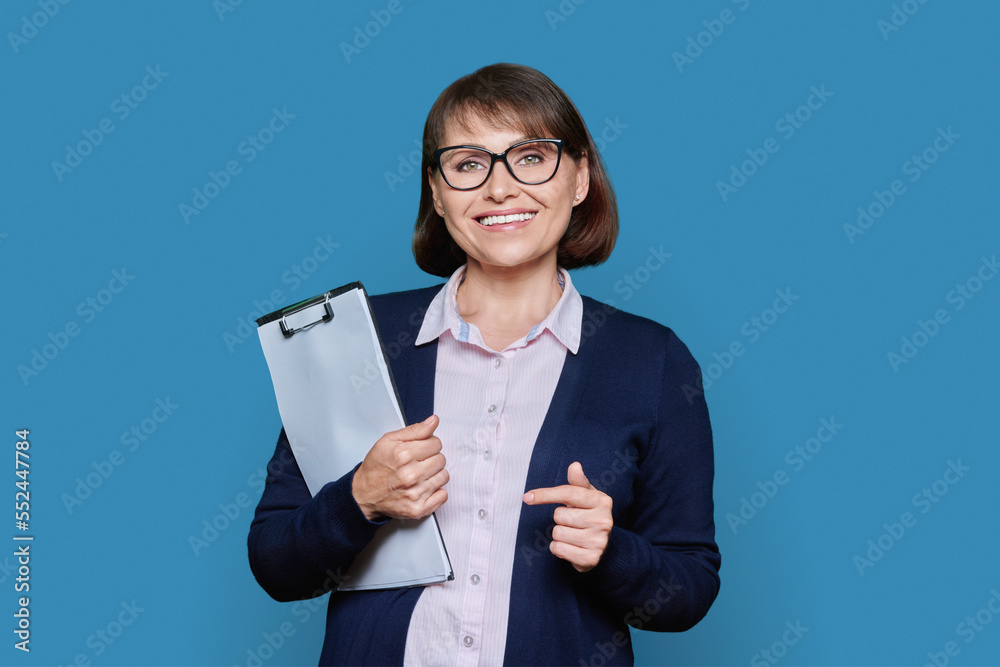 Middle age business woman with clipboard looking at camera on blue background Middle age business woman with clipboard looking at camera on blue background