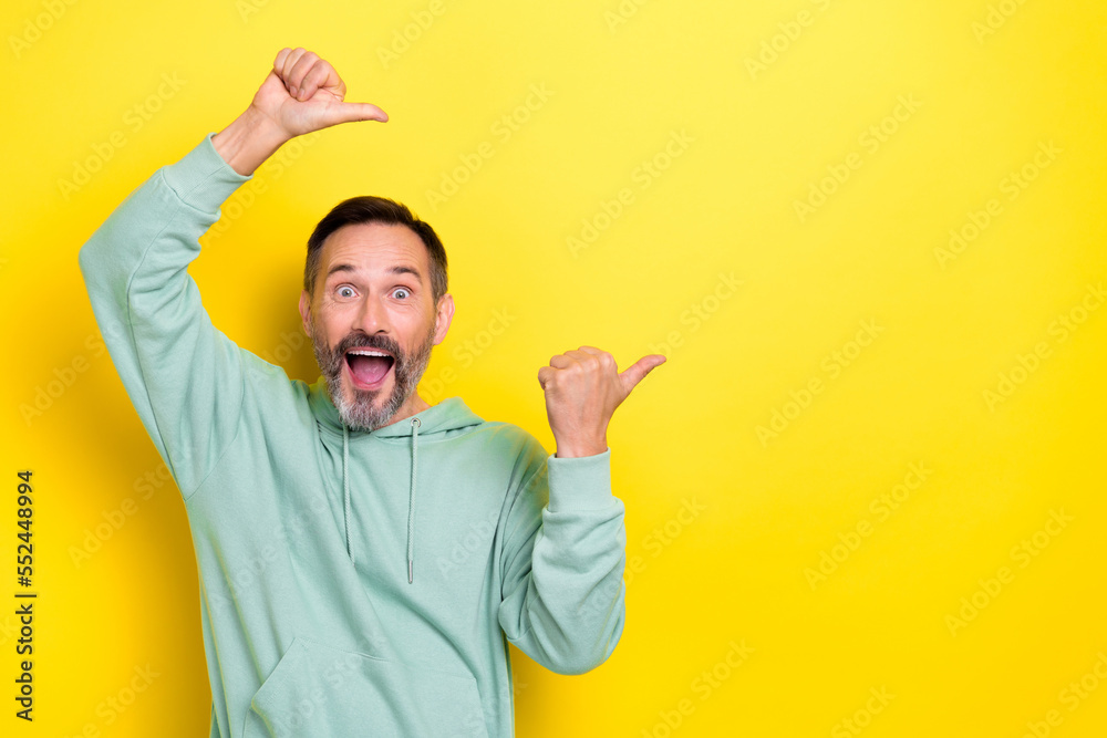 Portrait of impressed astonished positive man dressed green hoodie directing empty space open mouth isolated on yellow color background Portrait of impressed astonished positive man dressed green hoodie directing empty space open mouth isolated on yellow color background