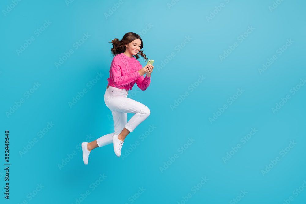 Full length photo of pretty adorable girl dressed knit pullover jumping high communicating device empty space isolated blue color background