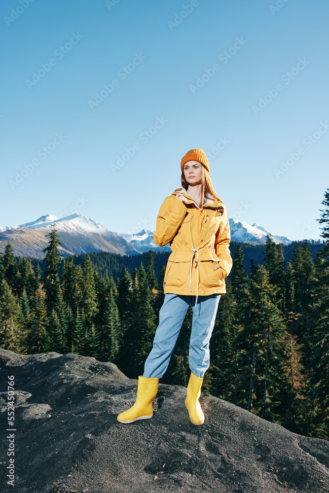 Naklejka premium Young woman with red hair full-length hiker in yellow raincoat and cap runs and walks on a mountain trip in the fall and hiking in the mountains at sunset freedom
