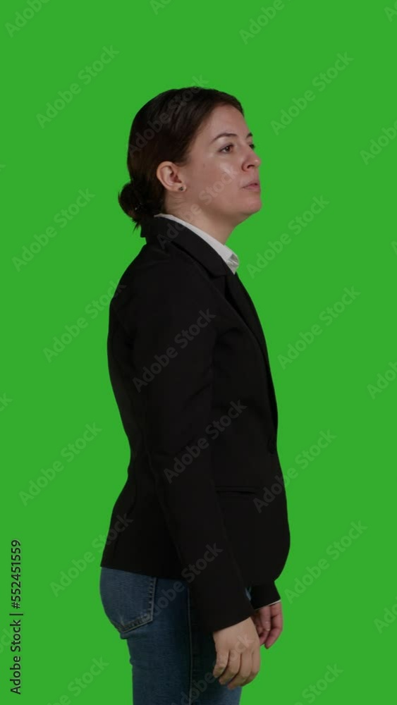 Vertical video: Profile close up of company employee raising hand and waving to call someone over, standing on isolated greenscreen backdrop. Young female worker asking and calling people to discuss Vertical video: Profile close up of company employee raising hand and waving to call someone over, standing on isolated greenscreen backdrop. Young female worker asking and calling people to discuss