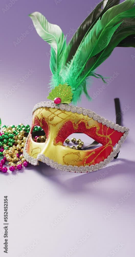Vertical video of masquerade mask with feathers and mardi gras carnival beads on lilac background