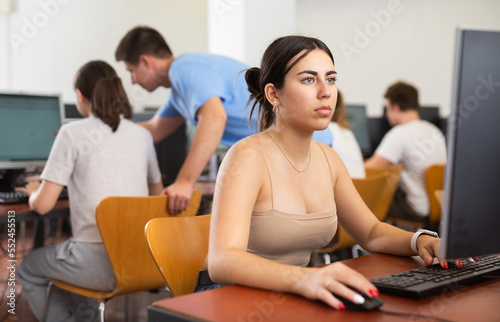 Focused young woman sitting at table in computer room in public library © JackF