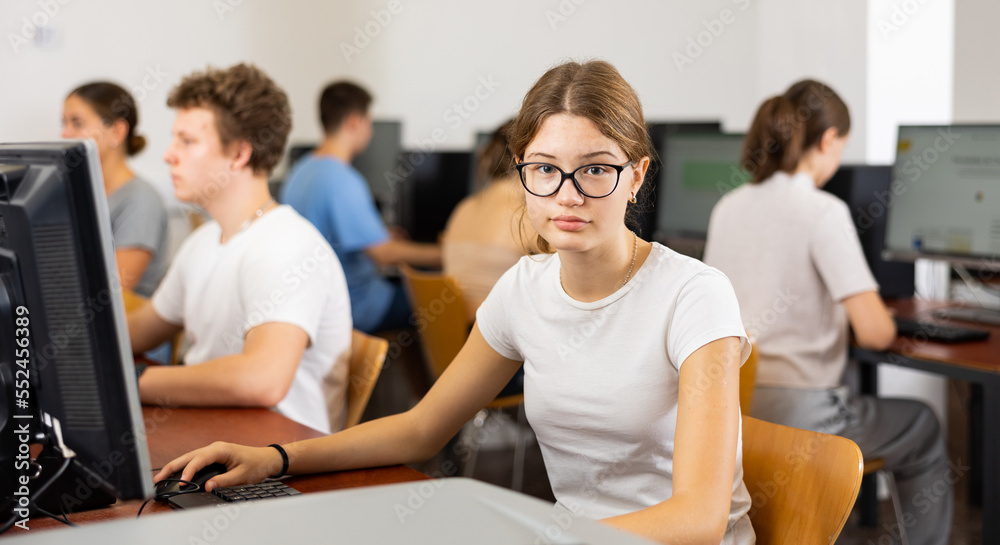 Fototapeta premium Focused female student in glasses using PC and studying computer science in the classroom