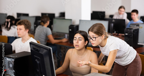 Teenager girl helps girlfriend solve problem on computer in a school class