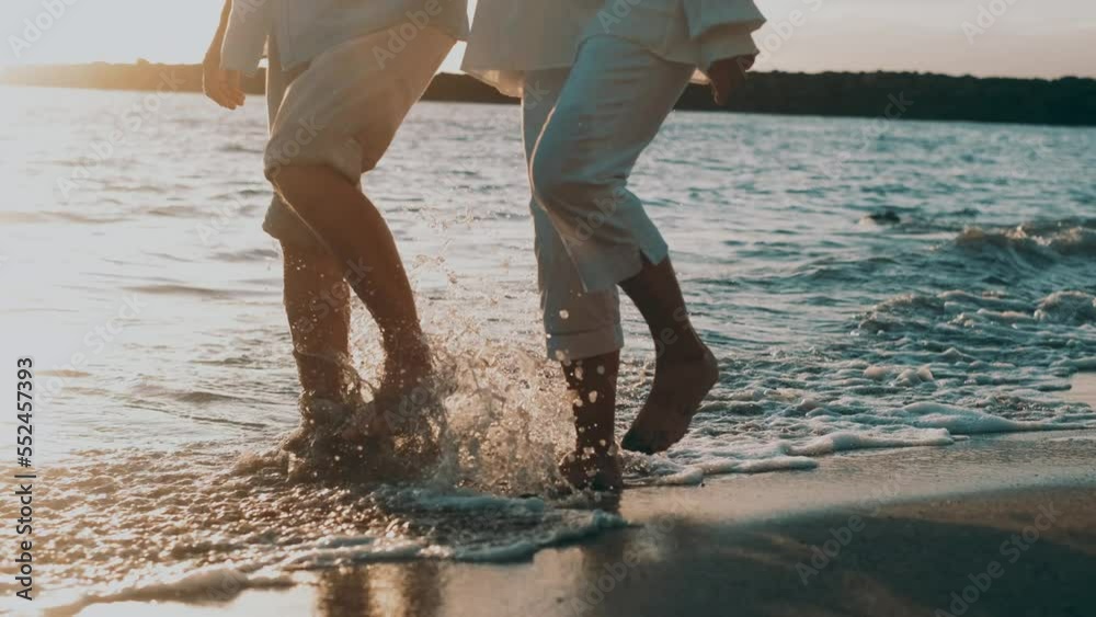Couple of old mature people walking on the sand together and having fun on the sand of the beach enjoying and living the moment. Two cute seniors in love having fun. Barefoot walking on the water