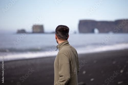 A man with his back turned looking at Dyrholaey from Reynisfjara black beach in Iceland
