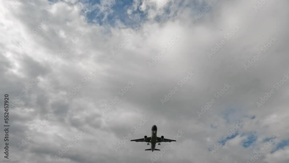 Wide low angle shot of airplane flying overhead against the background of white clouds Wide low angle shot of airplane flying overhead against the background of white clouds
