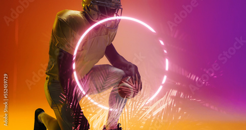 American football player with ball kneeling by illuminated circle shape and plants, copy space