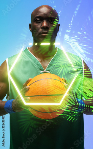 Portrait of african american basketball player with ball standing by illuminated hexagon and plants