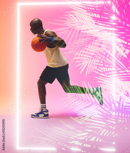 Side view of african american basketball player dribbling ball and running by rectangle and plants