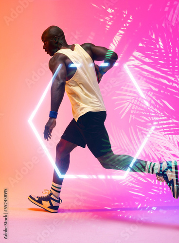 Side view of african american basketball player dribbling ball and running by hexagon and plants