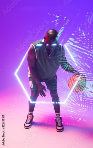 African american bald basketball player dribbling ball by illuminated hexagon and plants