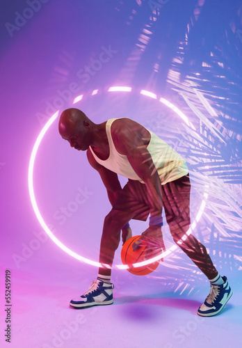 Bald african american basketball player juggling with ball by illuminated circle and plants